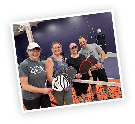 Four players smiling behind the net at Pickleplex Social Club
