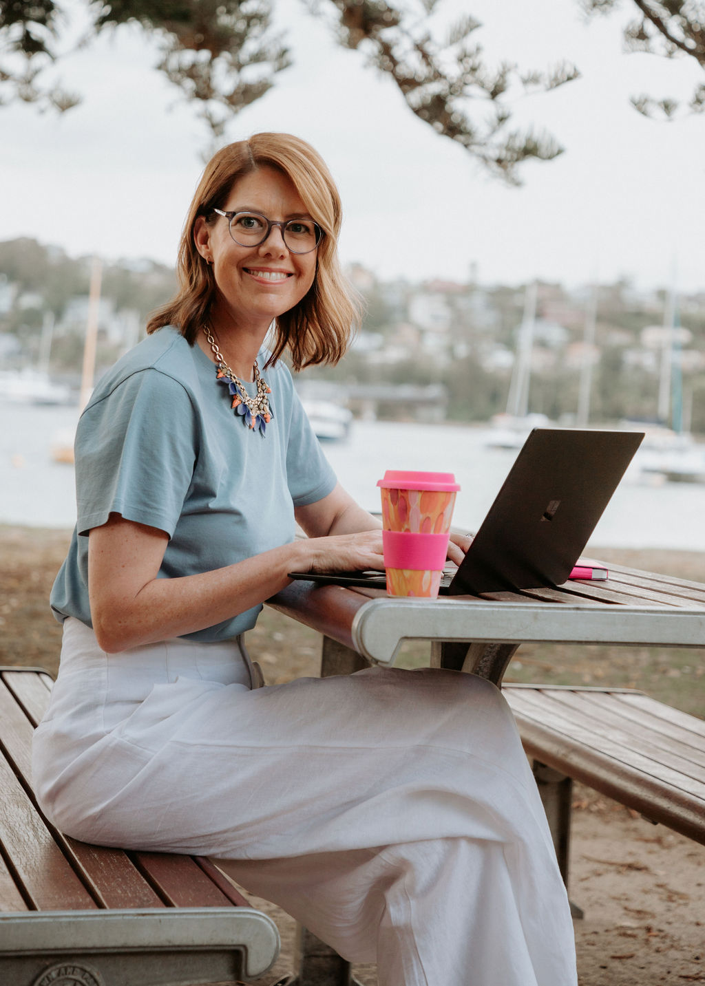 Carly Donovan working at a laptop outdoors by the water in Mosman