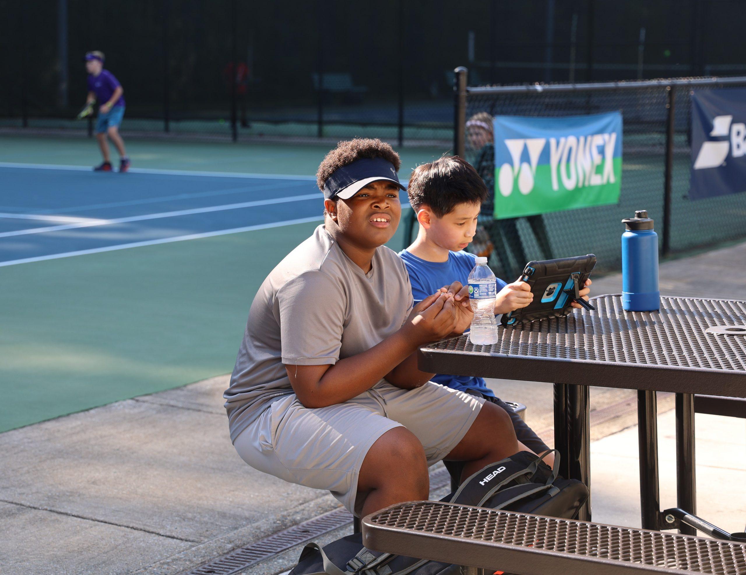 Junior tennis players reviewing match play and resting courtside