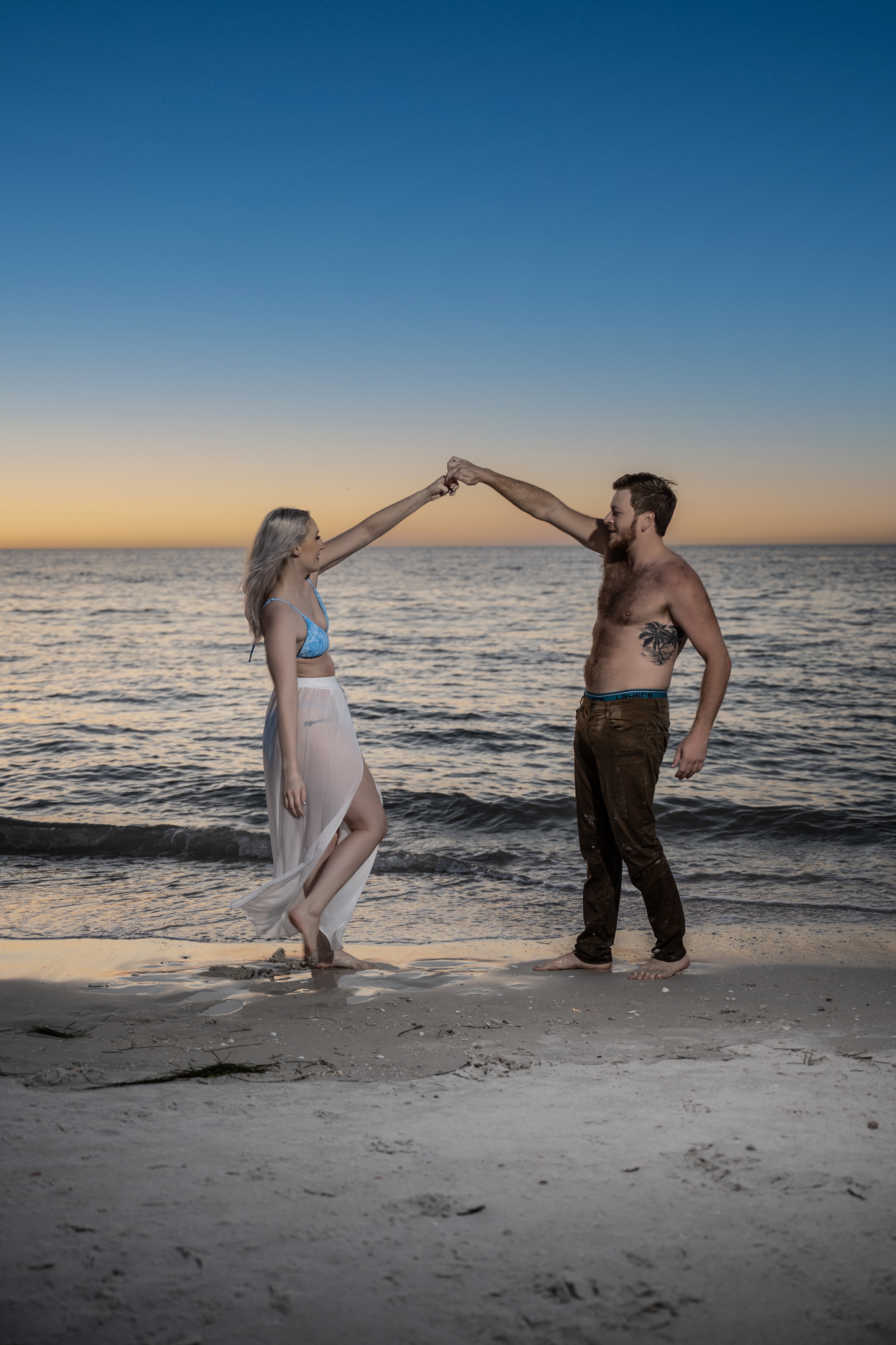 Couple dancing and twirling on the shoreline at sunset