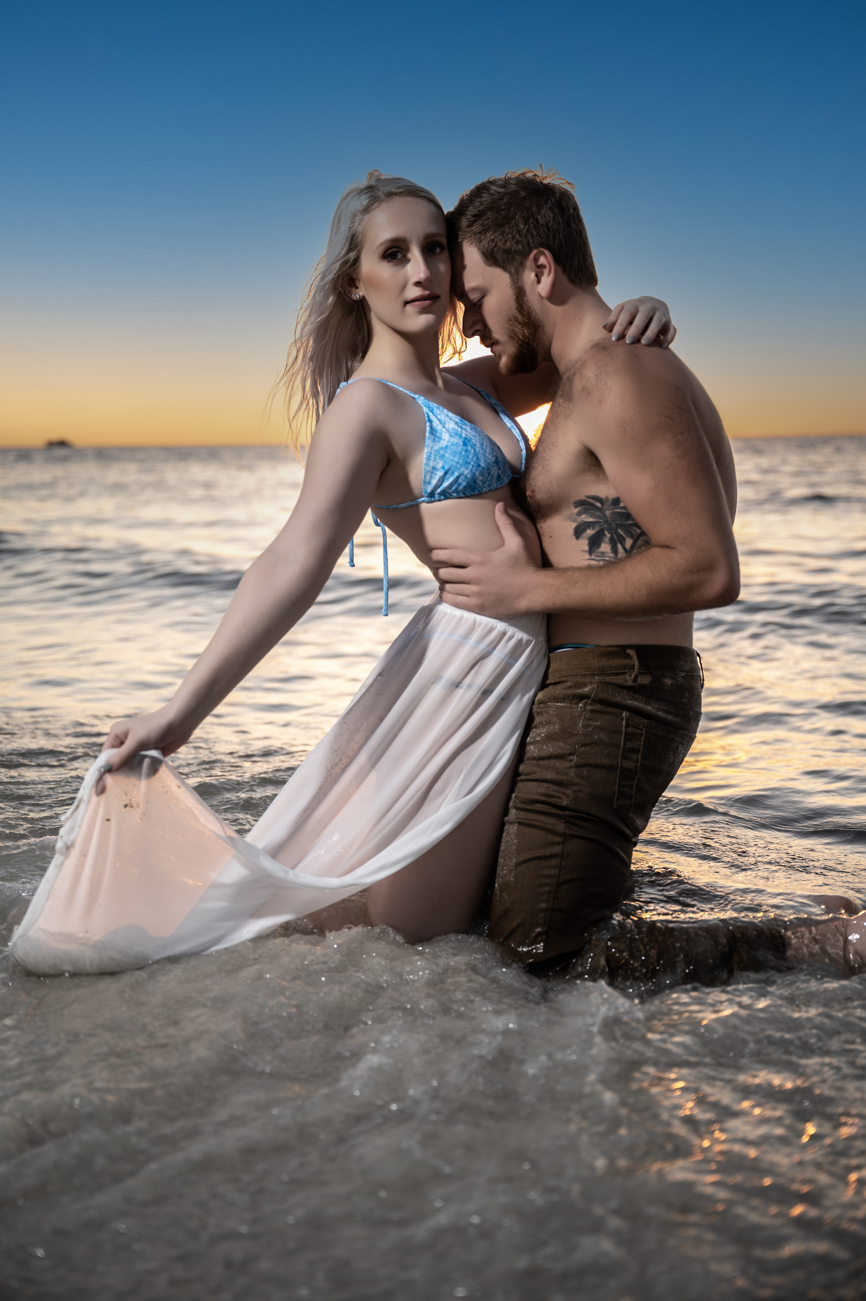 Romantic couple embracing in the ocean tide at golden hour