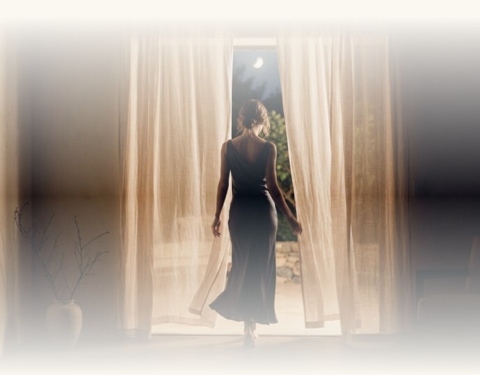 Woman in silk dress walking through sheer linen curtains into a moonlit garden