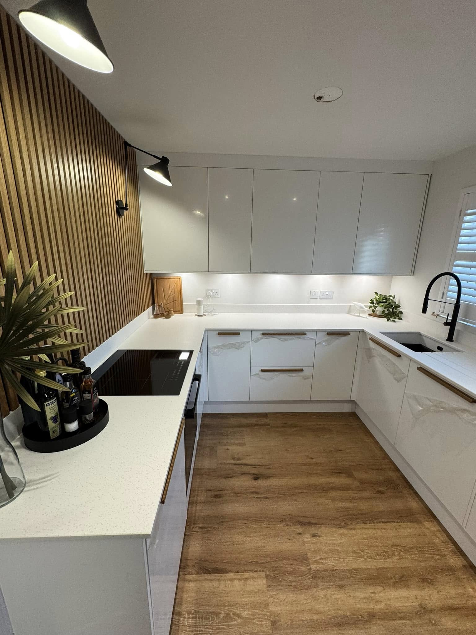 Contemporary white kitchen with timber slat feature wall, quartz worktops and recessed lighting by Diamond Kitchens & Bathrooms