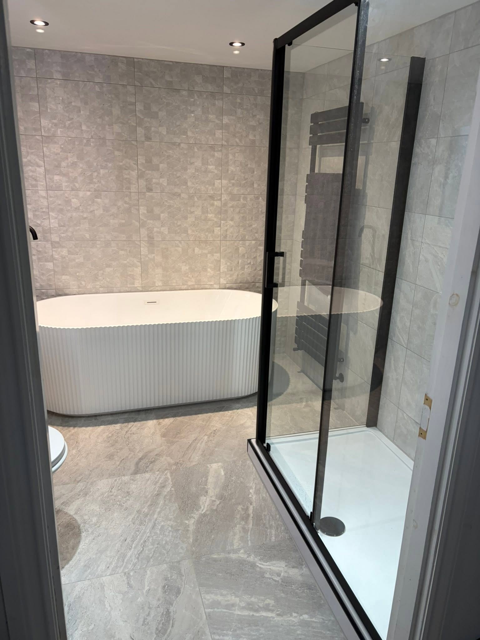 Luxury freestanding fluted bath and walk-in matte black framed shower with stone tiling by Diamond Kitchens & Bathrooms