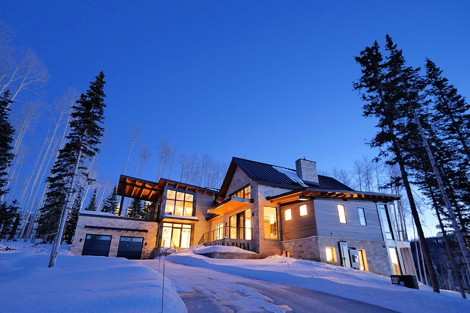 Twilight exterior of custom alpine residence nestled in snowy Telluride aspen forest