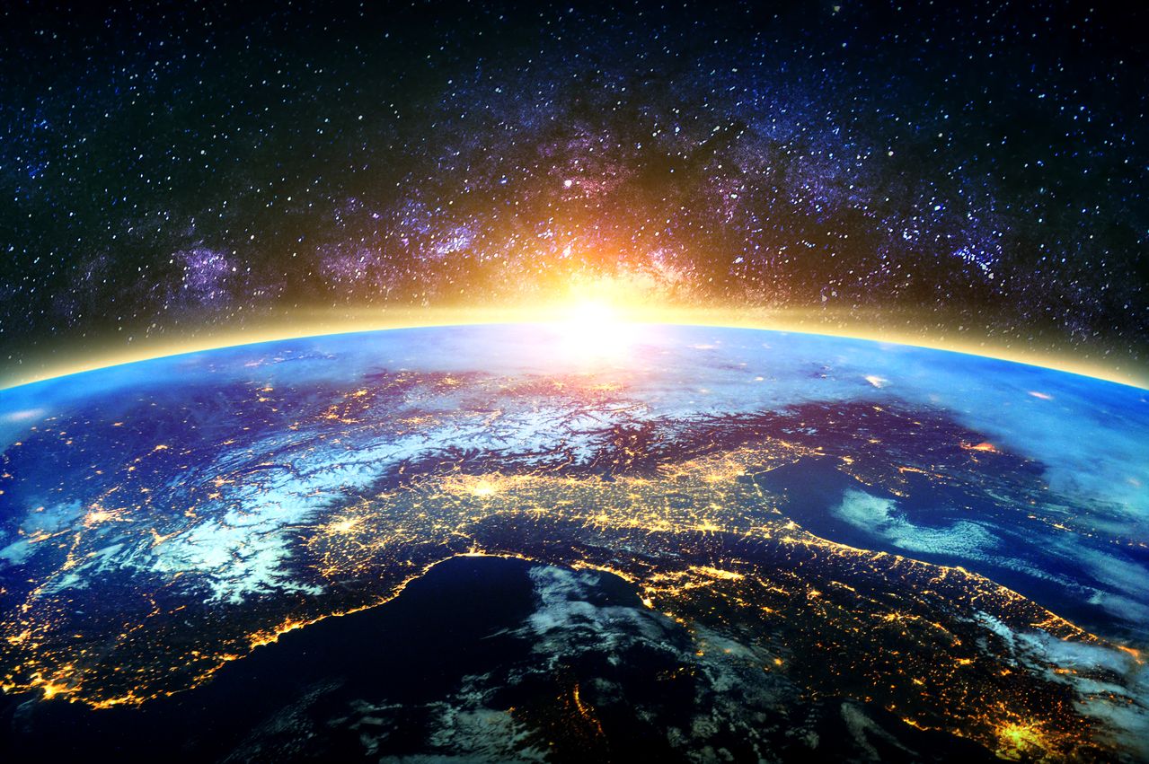 Earth from space with glowing sunrise over the curved horizon and city lights