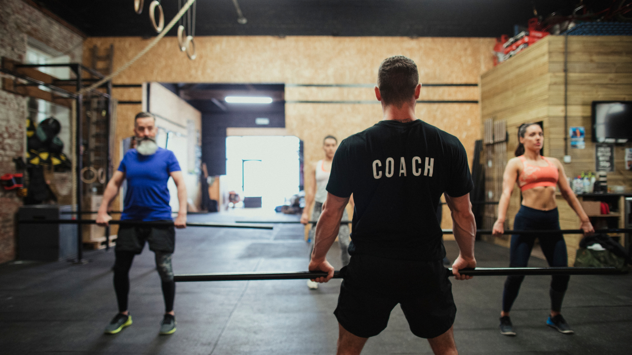 Coach qui corrige la posture d'un membre avec barre