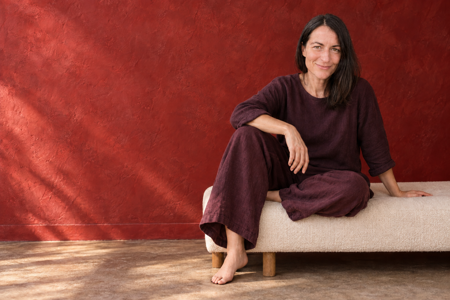 Lalena Rose seated comfortably in plum linen against a rich terracotta-red wall