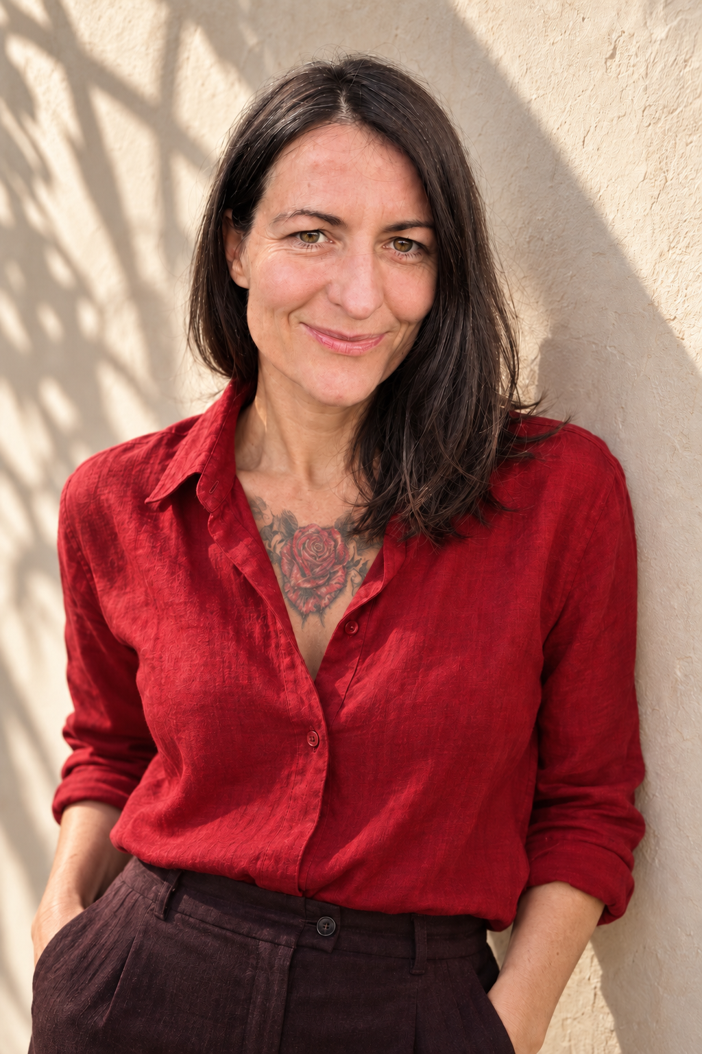 Portrait of Lalena Rose in a vibrant red linen shirt smiling warmly against a sunlit wall
