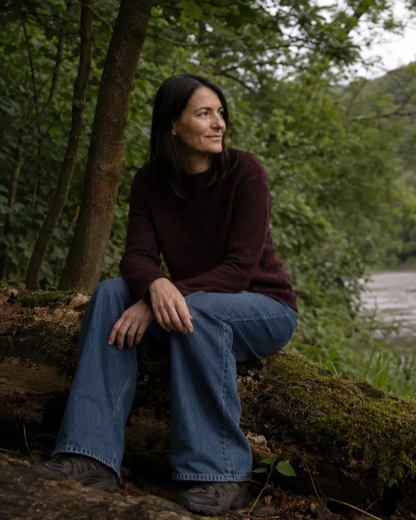 Portrait of Lalena Rose sitting on a mossy log by the river in a forest