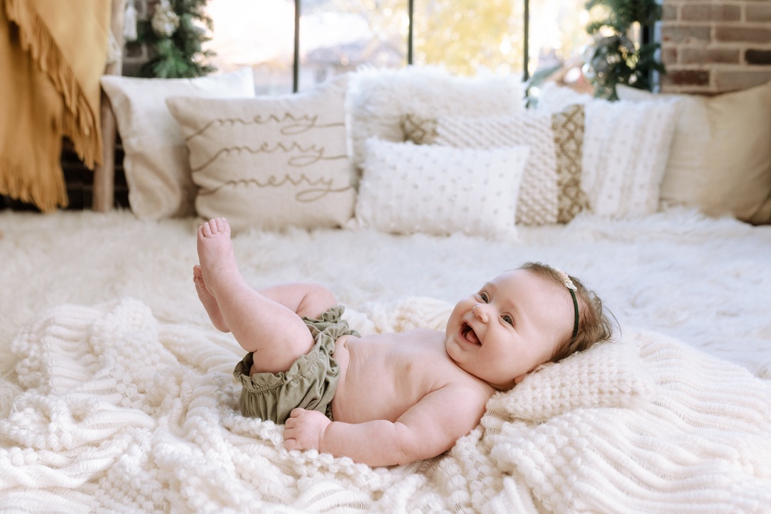 Smiling baby laughing on cream holiday bed with merry pillows