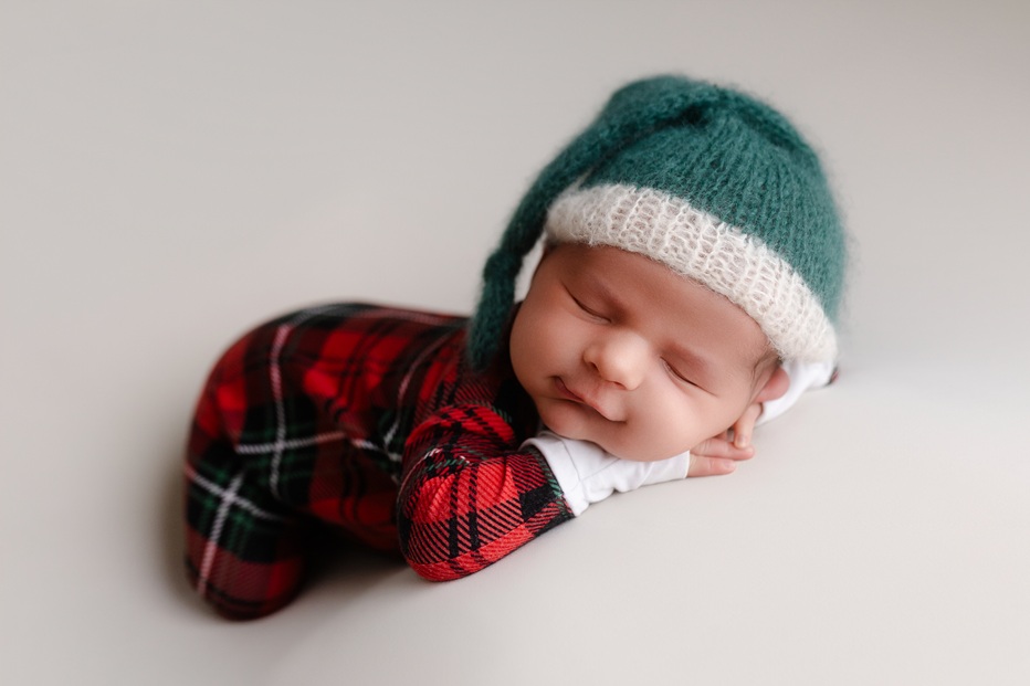 Sleeping newborn in plaid holiday outfit and green knit elf hat