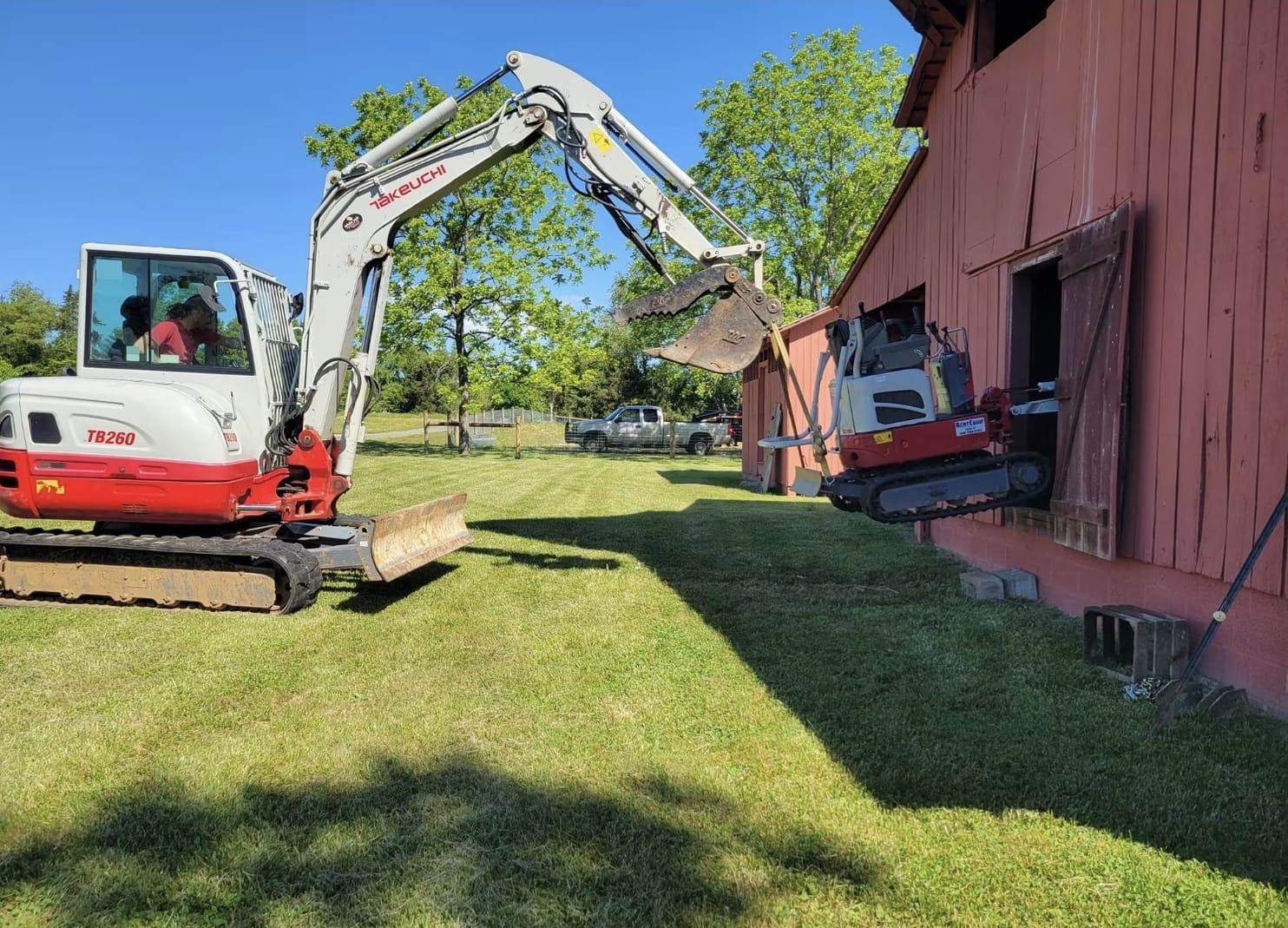 Tracked excavator positioning equipment beside a red estate barn during property access and site preparation