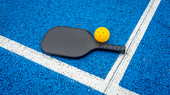 Pickleball paddle and yellow ball resting on a textured blue court surface built by Henderson pickleball court builders in Nevada