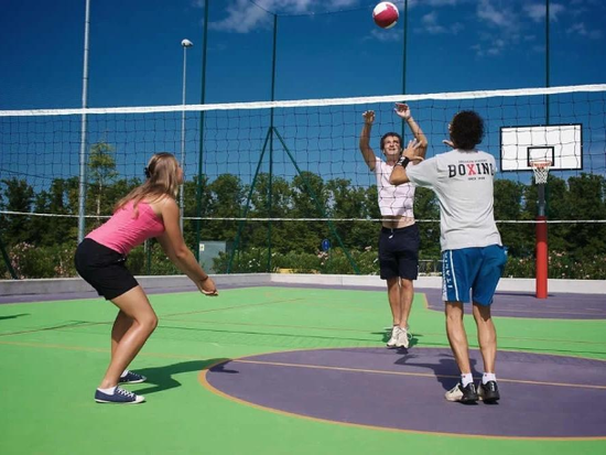 Players jumping to hit a volleyball over a net on a colorful outdoor court during a court builder service in Henderson, NV
