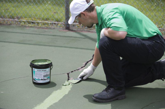Technician repairing cracks on a green sport court surface with sealant during a court builder service in Henderson, NV