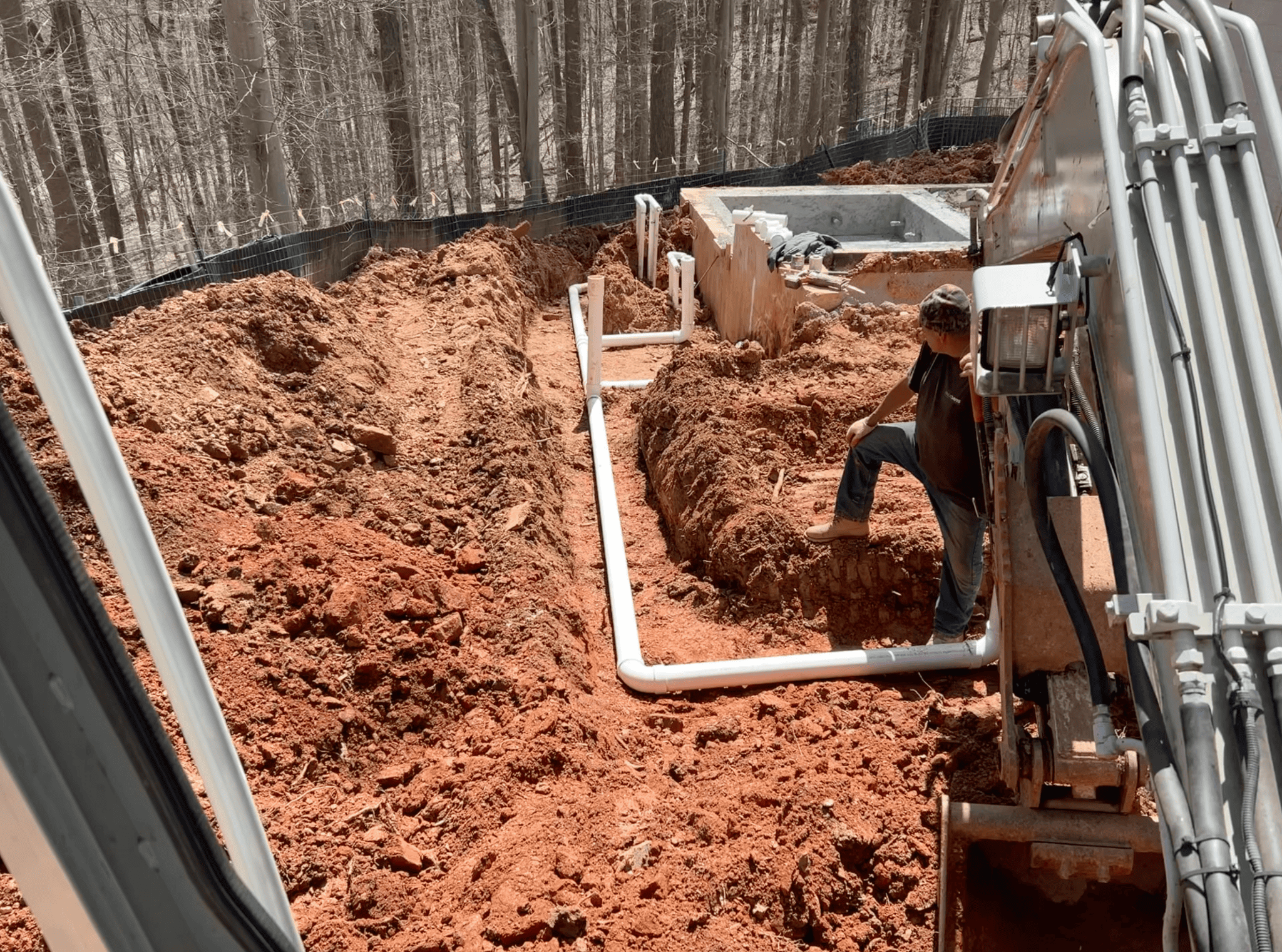 Excavation site work showing foundation digging, trenching, plumbing conduit, and excavator operator on site in Montgomery County, MD