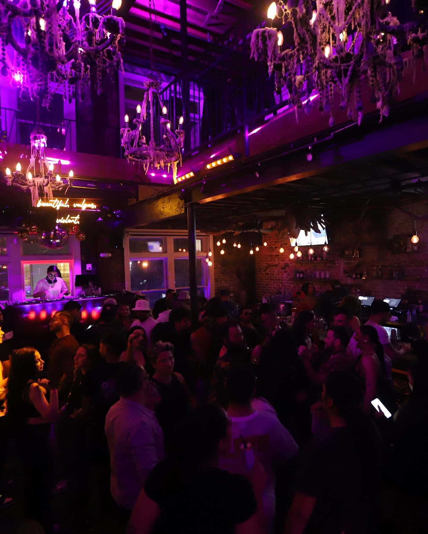 Packed two-story party at McQueens with gothic chandeliers and exposed brick