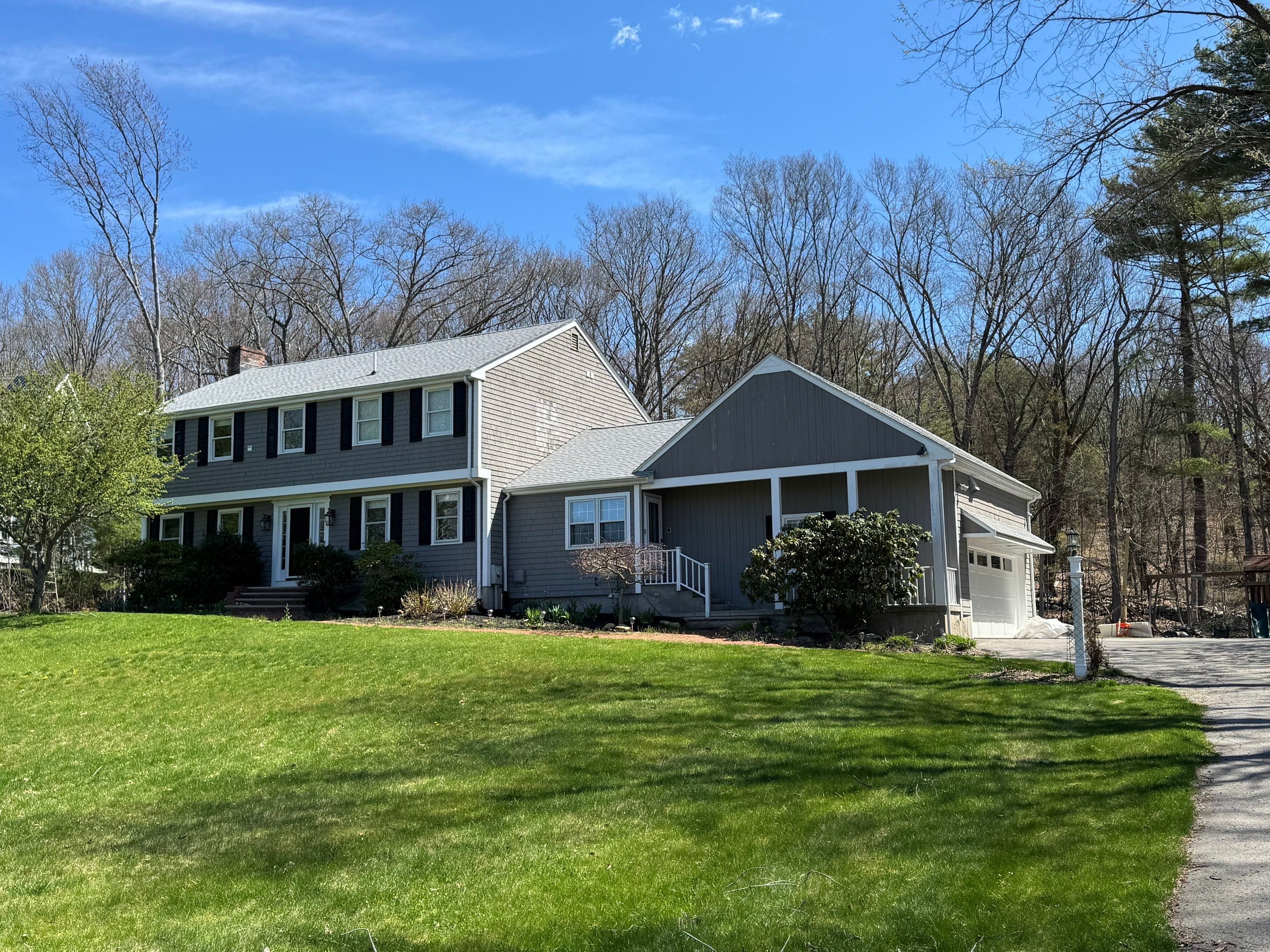 Completed exterior painting of a Massachusetts home with warm grey shake siding, black shutters, white trim, and attached garage
