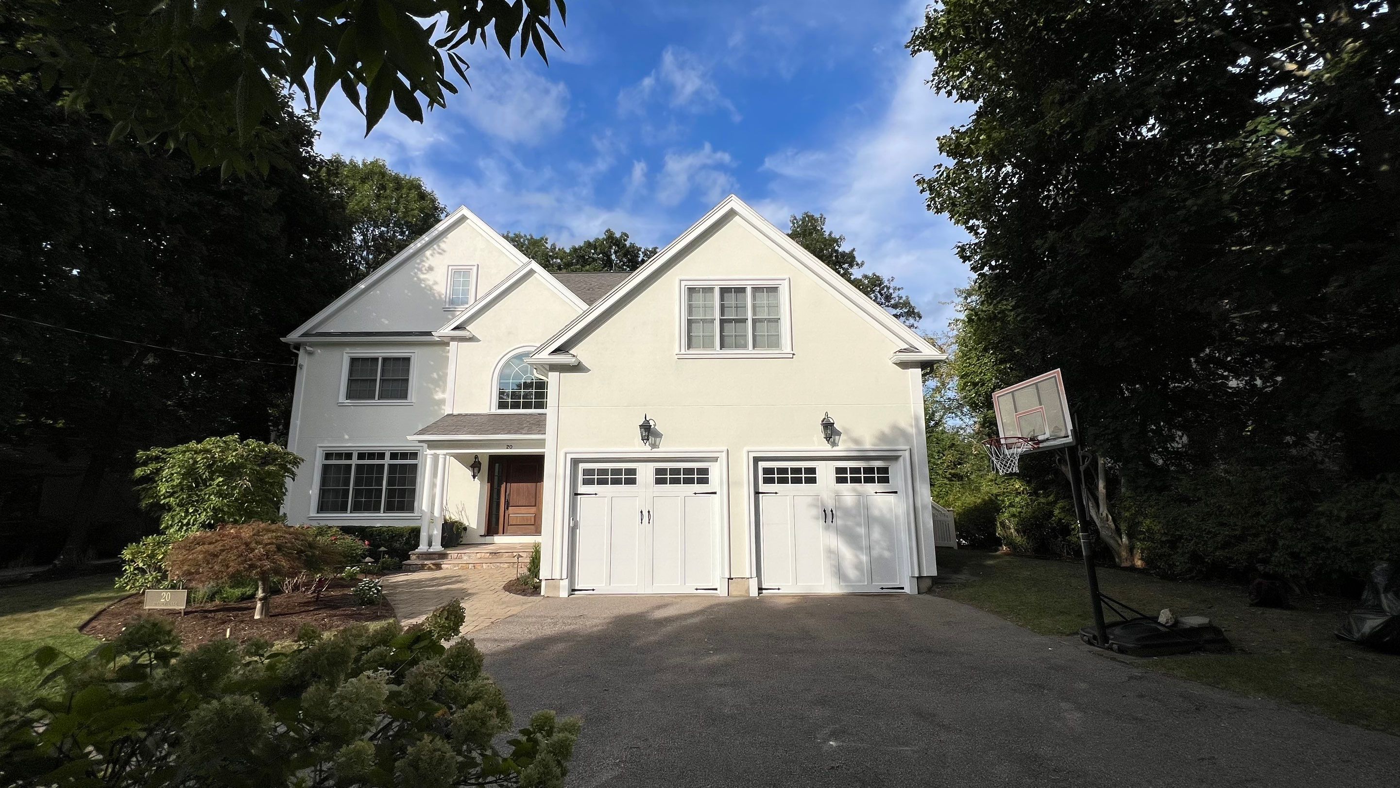 Freshly painted luxury two-story home in warm off-white with white multi-pane windows, arched entry, and white carriage house garage doors