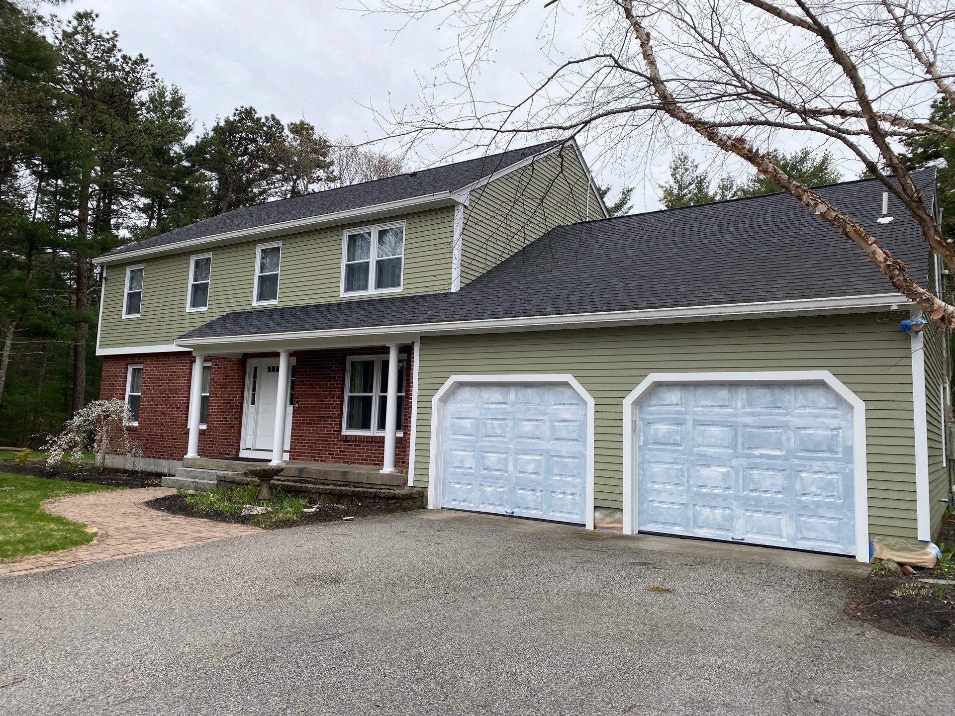 Massachusetts two-story home with fresh sage green siding, red brick facade, white columns, and garage