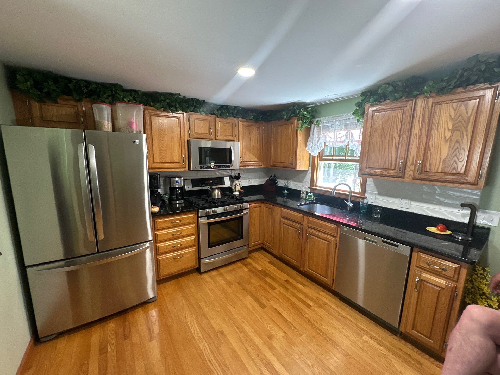 Before cabinet painting: dated golden oak kitchen cabinets with dark granite countertops and ivy above cabinets