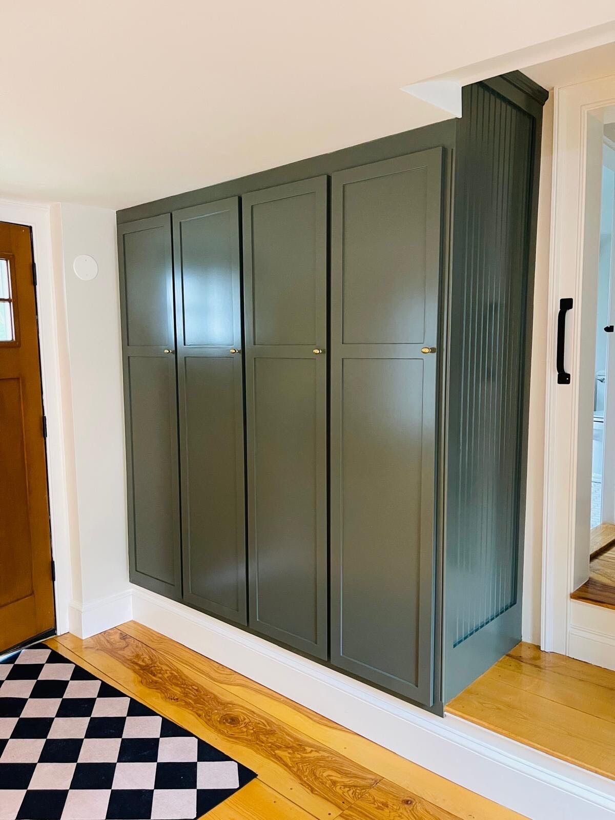 Completed floor-to-ceiling built-in pantry painted in deep forest green with delicate brass knobs and vertical beadboard side panels