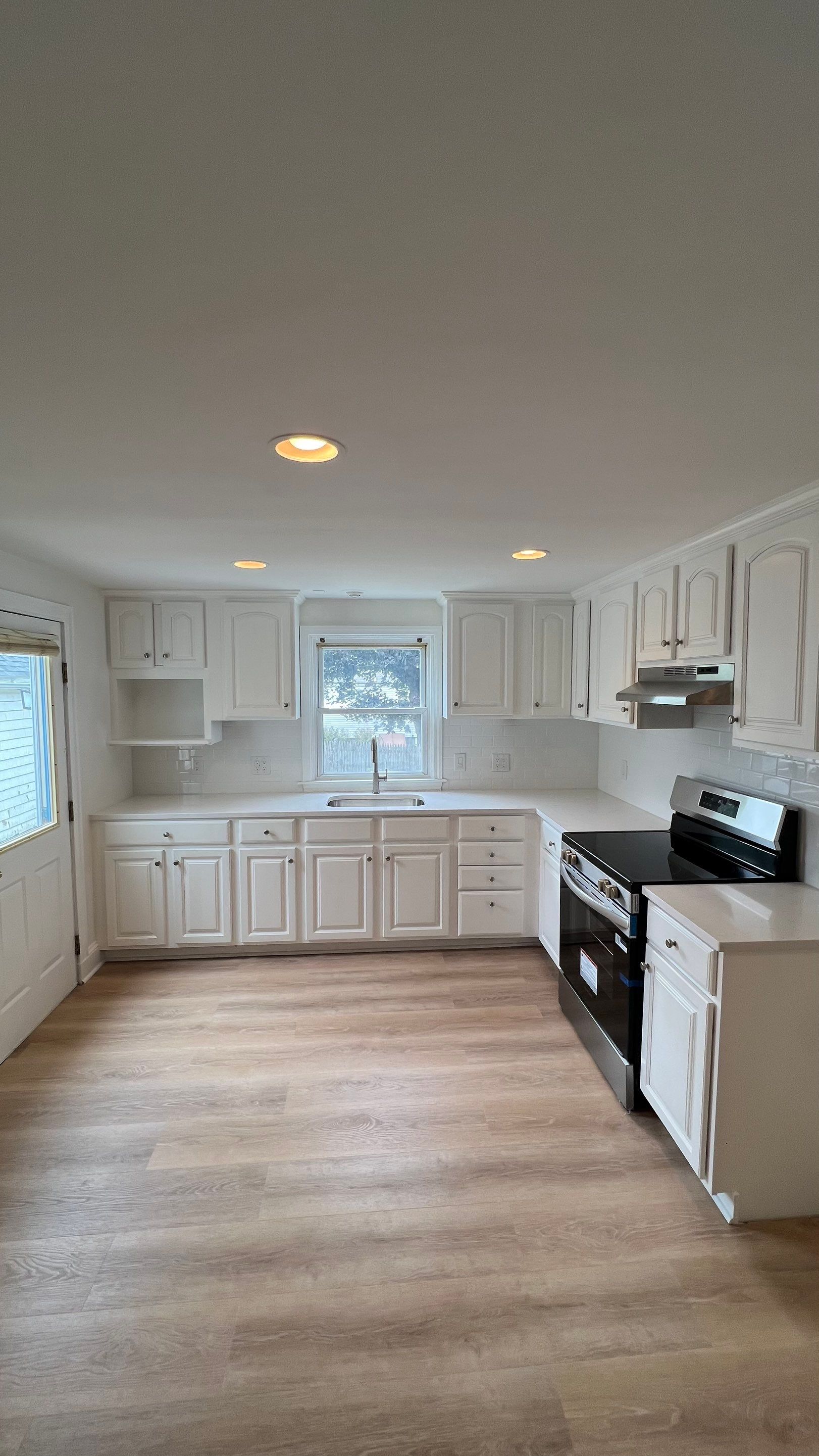 Completed full kitchen cabinet refinishing in bright white with arched panel doors, recessed lighting, and clean quartz counters