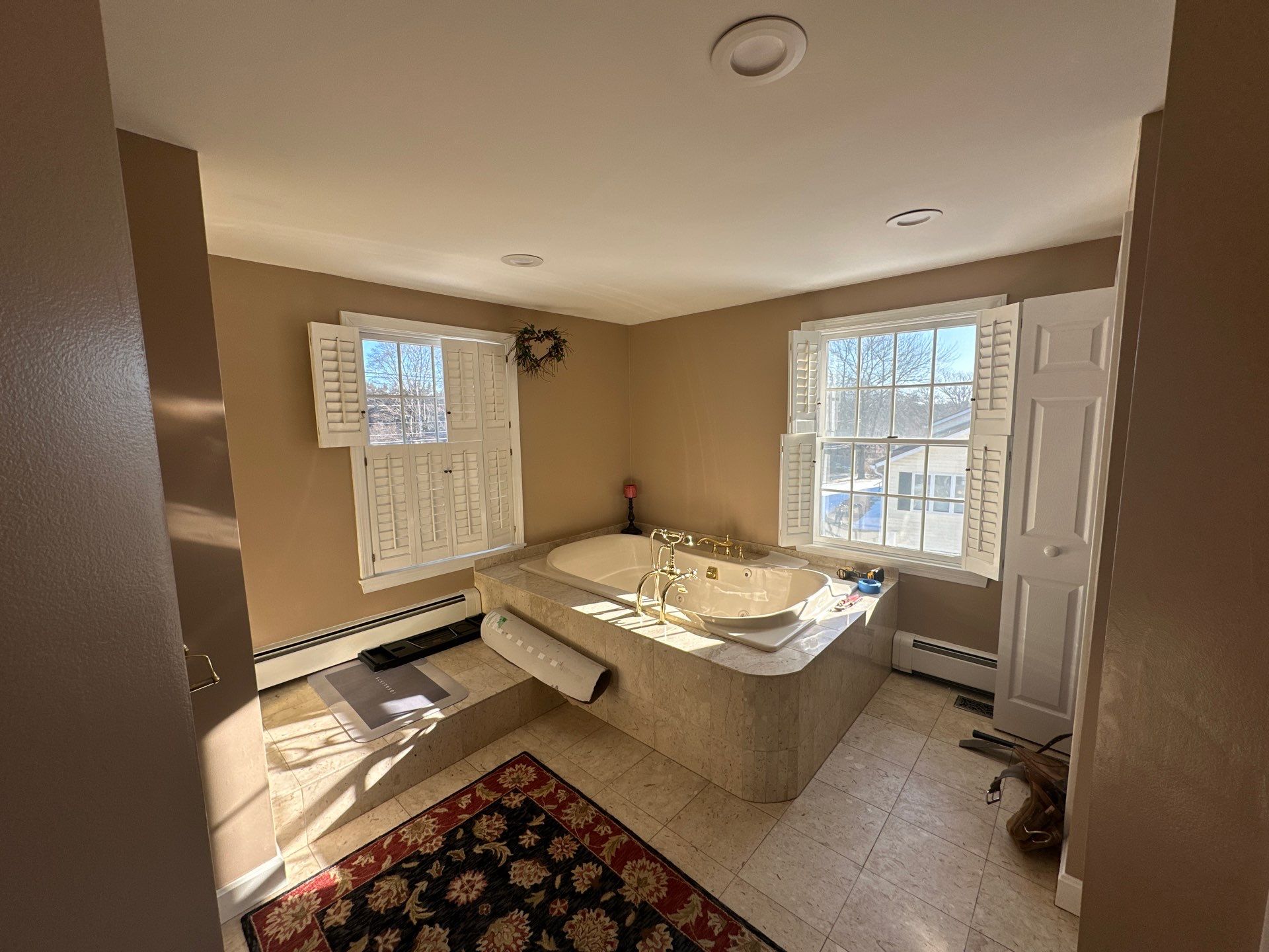 Before remodel: dated beige corner jacuzzi tub with brass fixtures and brown walls