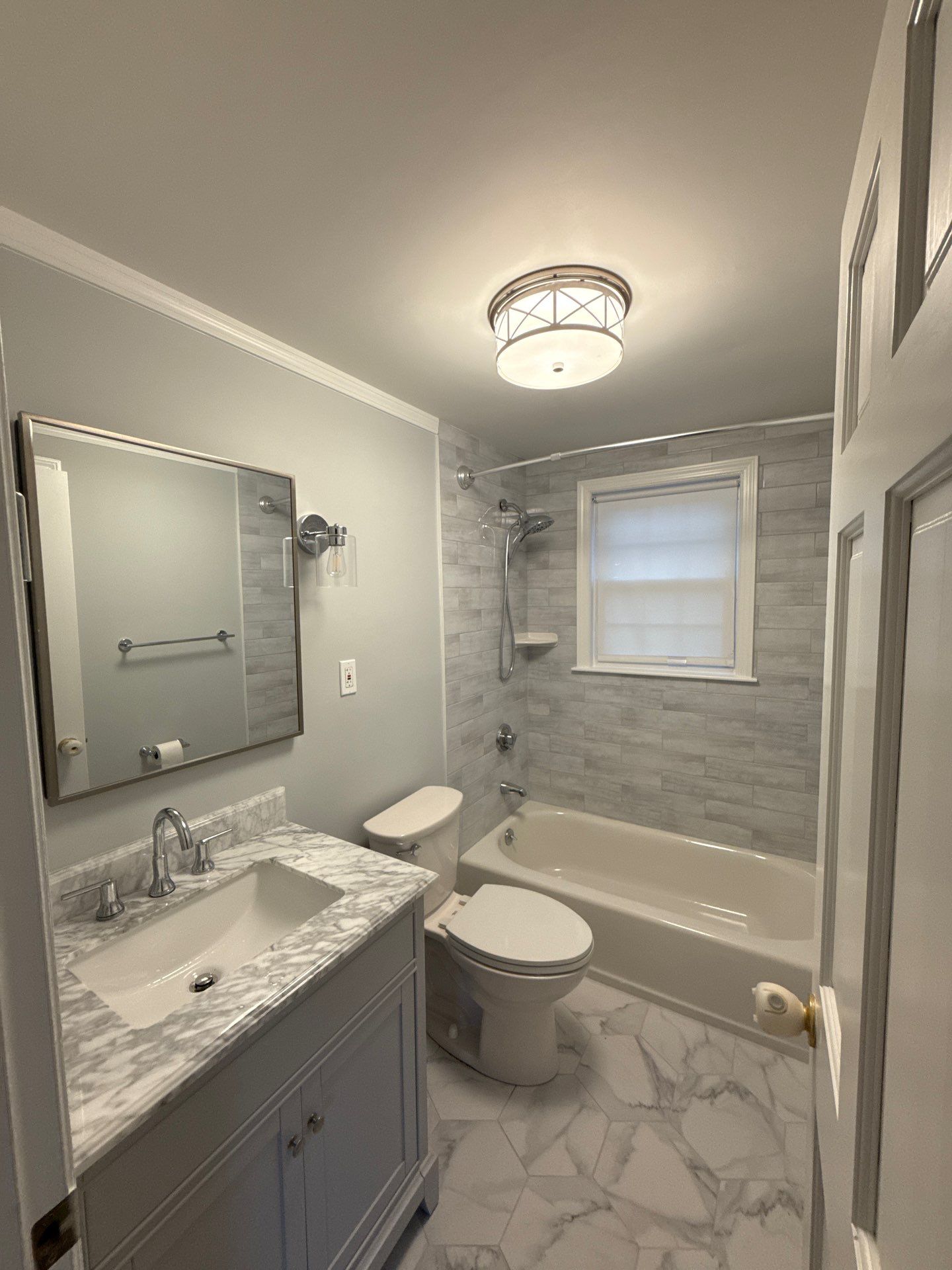 Completed modern full bathroom remodel with marble top vanity and neutral subway tile shower tub surround