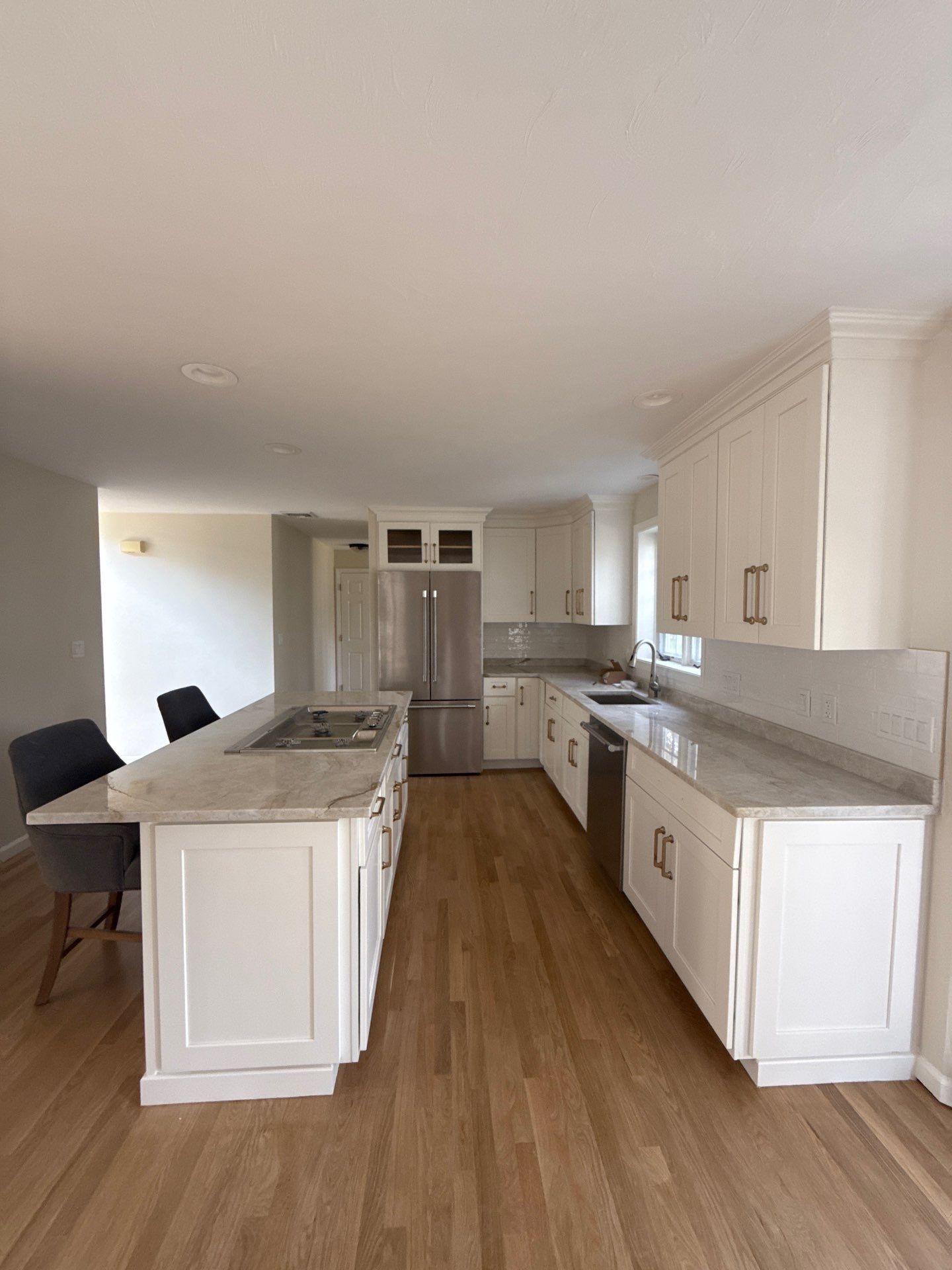 After remodel: bright open kitchen with white shaker cabinets, quartz island with cooktop, brass hardware, and hardwood floors