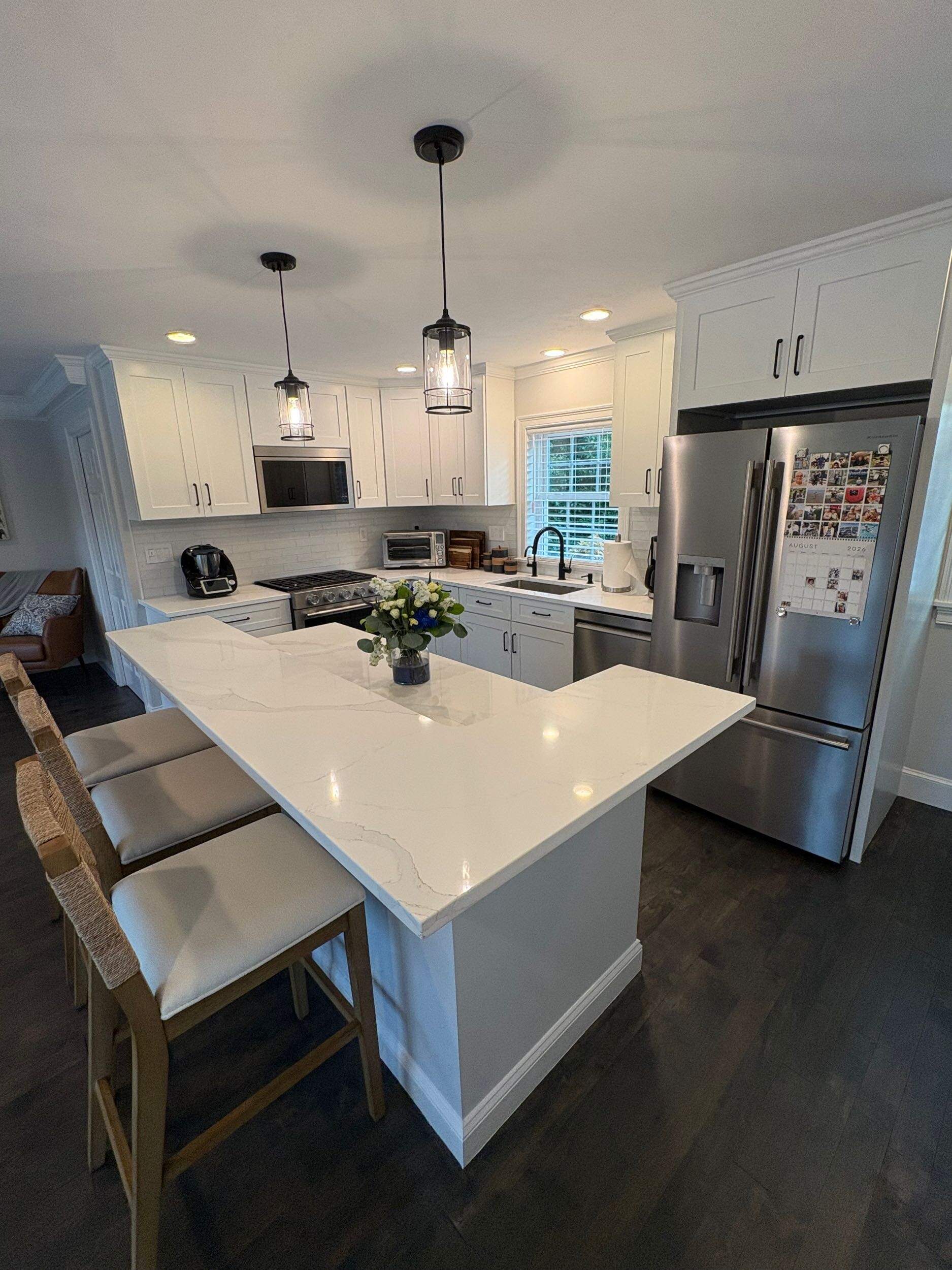 Completed kitchen renovation with large quartz peninsula island, white shaker cabinets, and pendant lights