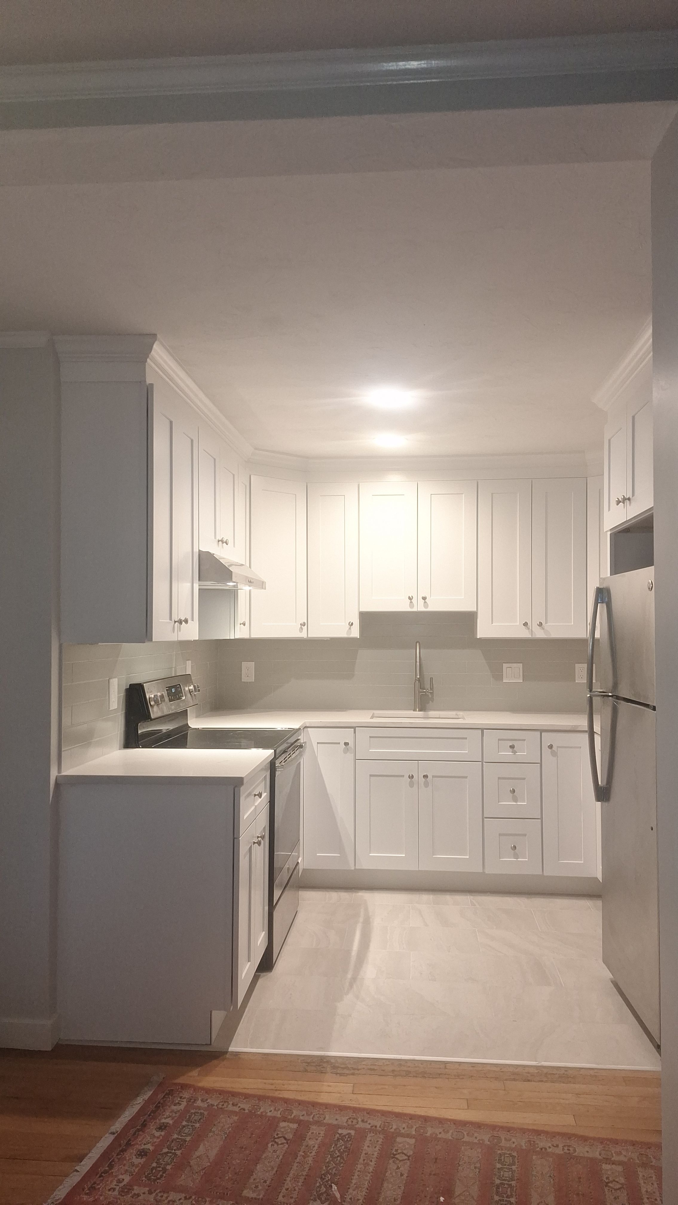 Completed kitchen renovation with full height white shaker cabinetry, stainless steel appliances, and large format tile floor