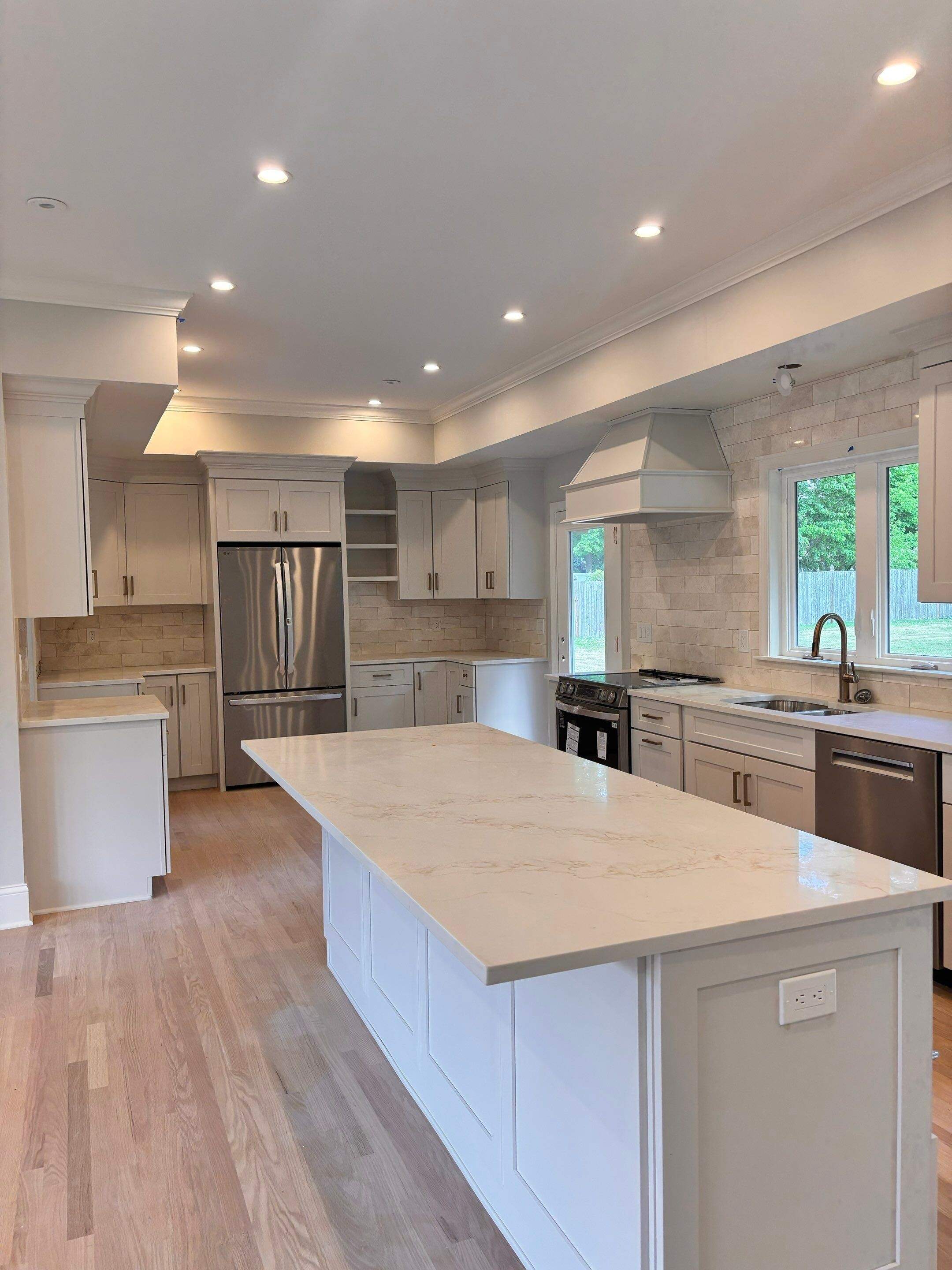 Completed open concept kitchen remodel with large center island, custom range hood, and tile backsplash