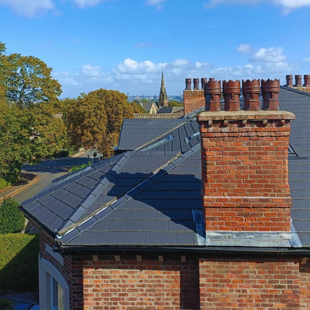 Rooftop view of Wirral red brick chimneys and slate roofs with distant church spire under blue sky