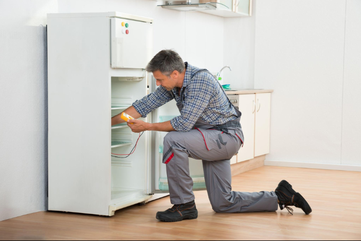 Repair technician kneeling beside a refrigerator and checking the lower compartment during an appliance repair service in Millcreek, UT