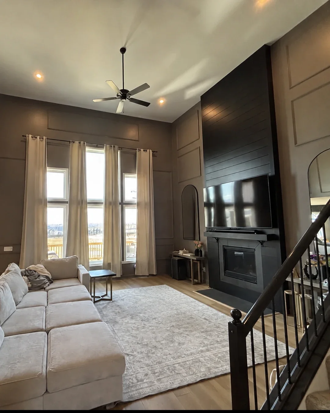Finished two-story living room interior painting with black shiplap fireplace accent wall, high ceiling, tall windows, and decorative wall molding completed by Quality Painters