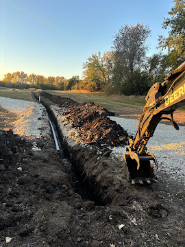 Excavator digging a water line trench beside a gravel drive in Northeast Kansas
