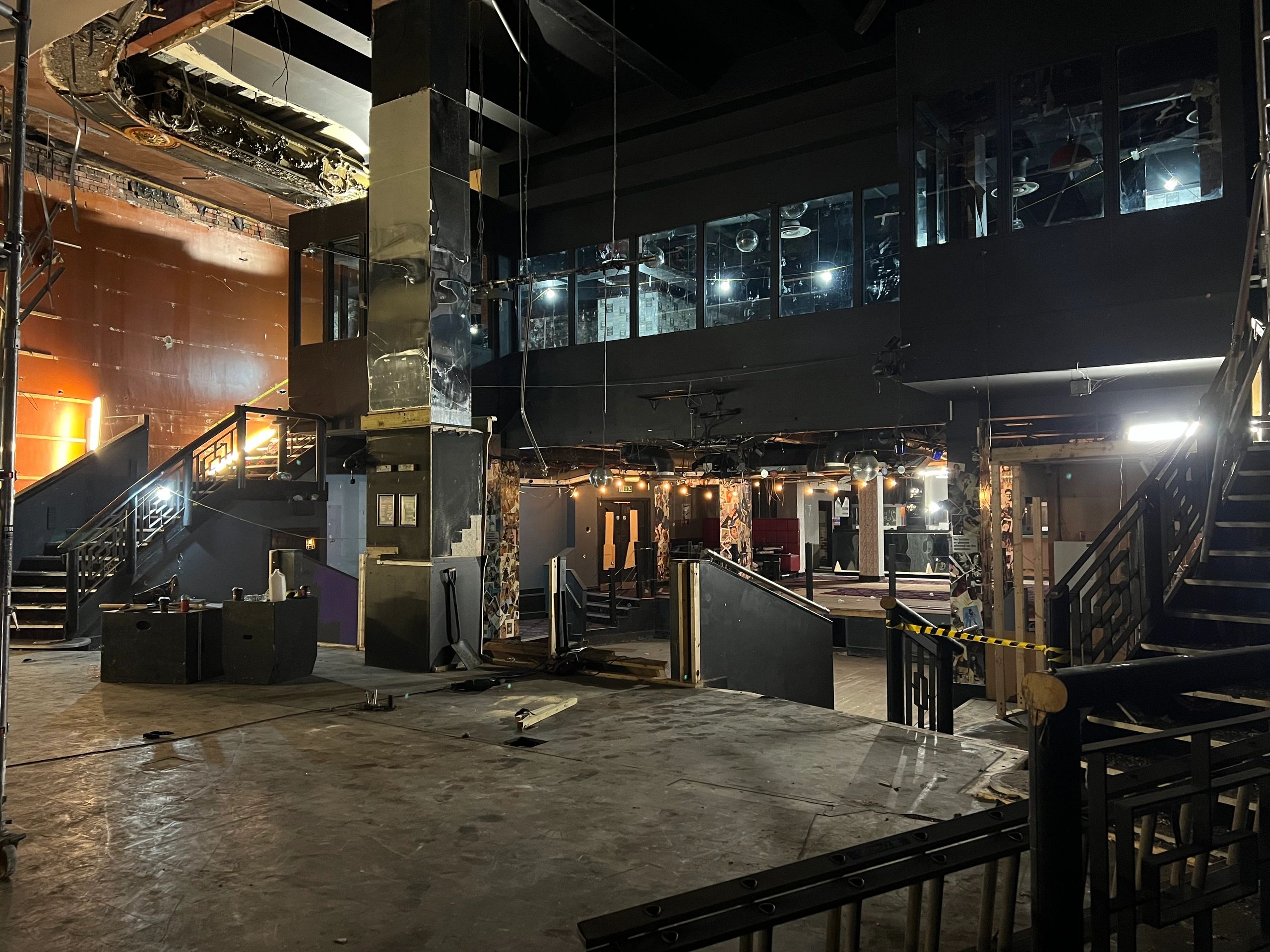 Interior of an empty, dimly lit nightclub or event space with stairs and a mezzanine level.
