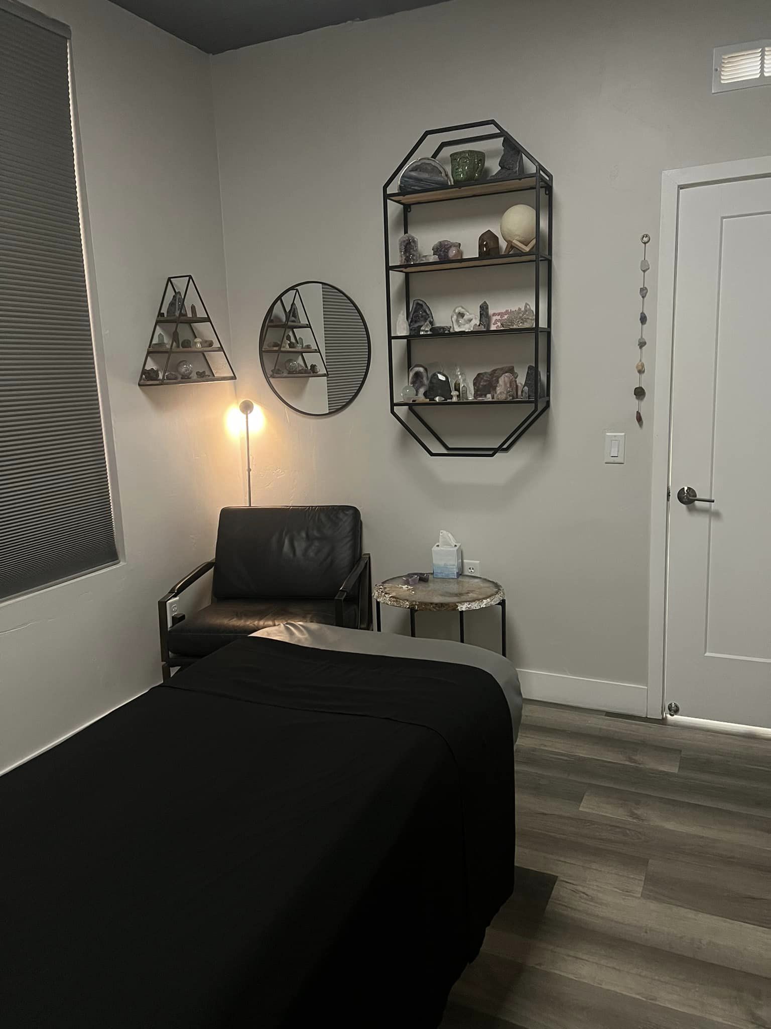 Tranquil treatment room with massage table, crystal display shelves, soft warm lamp, and leather chair