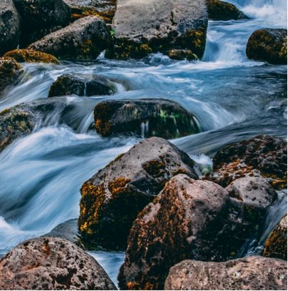 Rushing mountain stream flowing over sunlit mossy river rocks