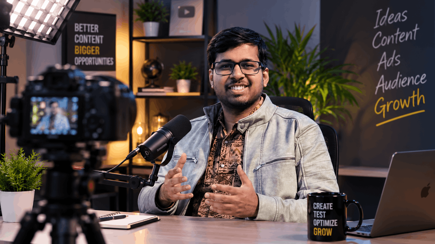 Creator recording video content in studio setup with camera, microphone, and chalkboard outlining ideas, content, ads, and audience growth