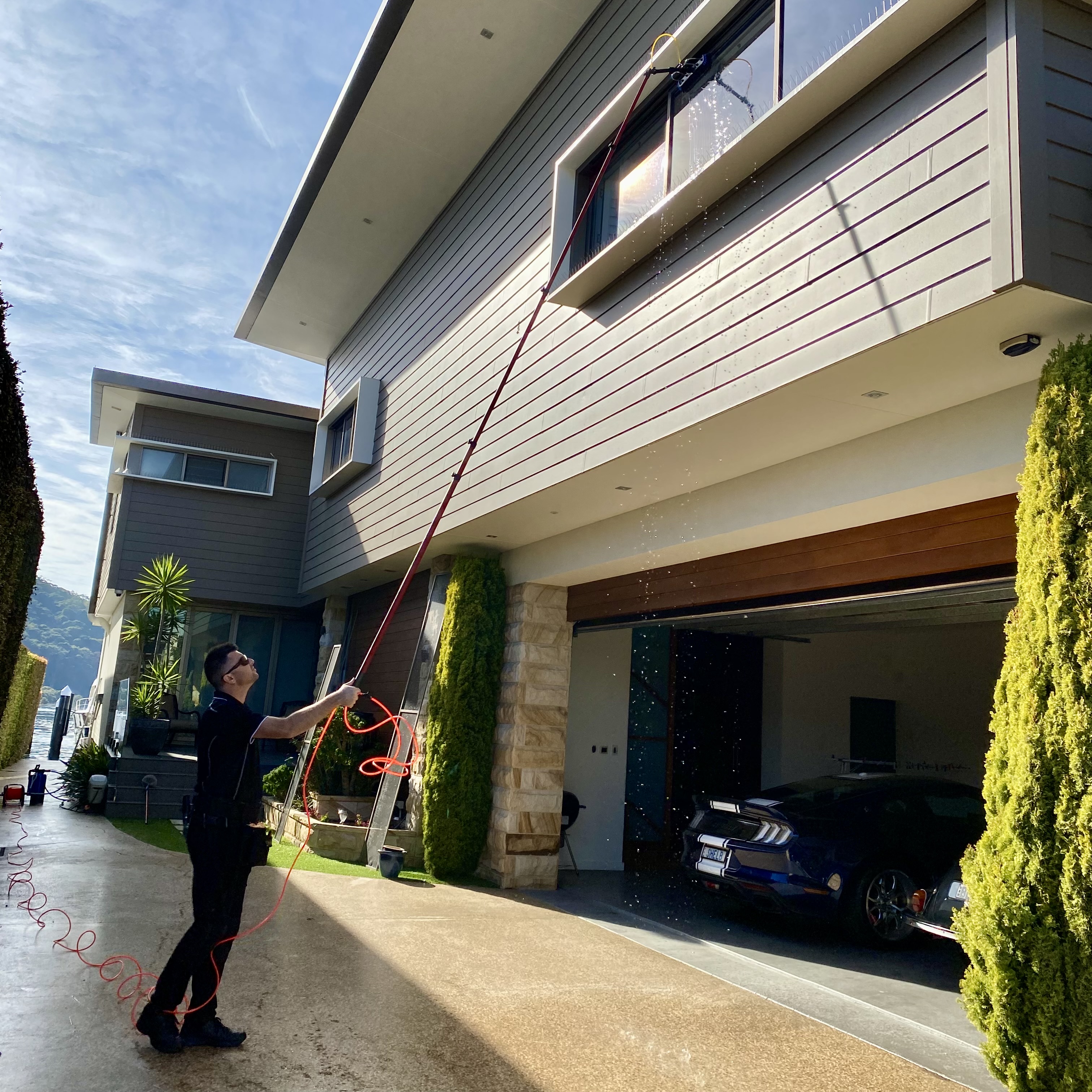 A professional window cleaner using a high-reach water-fed pole system on second-storey commercial residential windows
