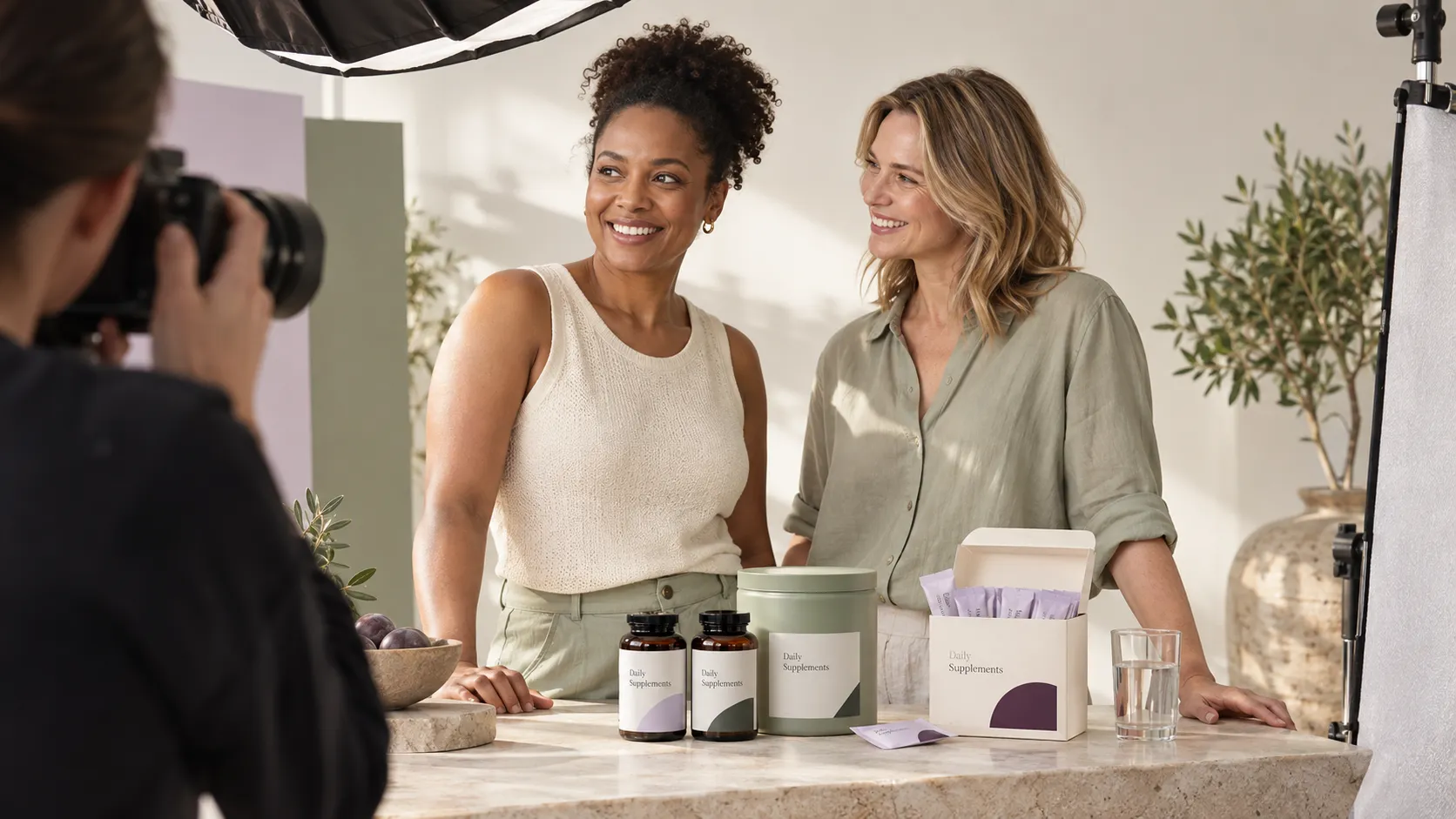 Two wellness brand founders at a studio campaign shoot reviewing daily supplement packaging in sage, plum and ivory tones.
