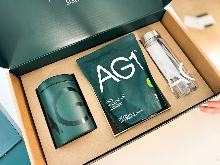 AG1 welcome kit unboxing showing the branded green canister, daily nutrition pouch, and shaker bottle in custom unboxing packaging.