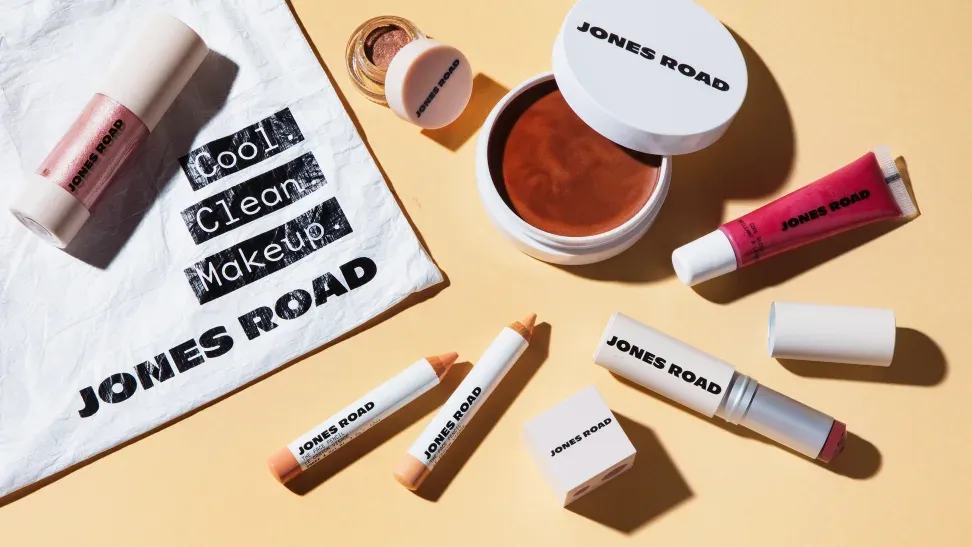 Jones Road product collection featuring makeup trios, face pencils, and lip sets arranged on a warm studio surface.