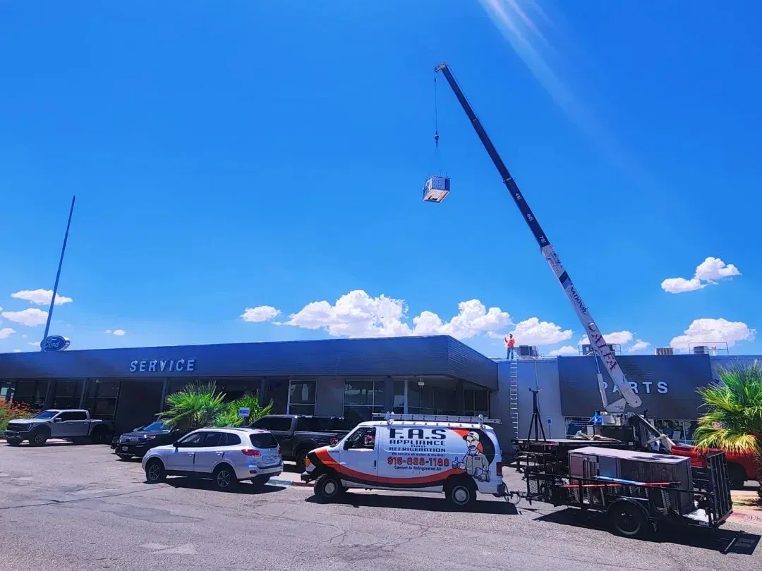 F.A.S work van and crane lifting rooftop HVAC unit at Ford dealership service center under sunny El Paso blue sky