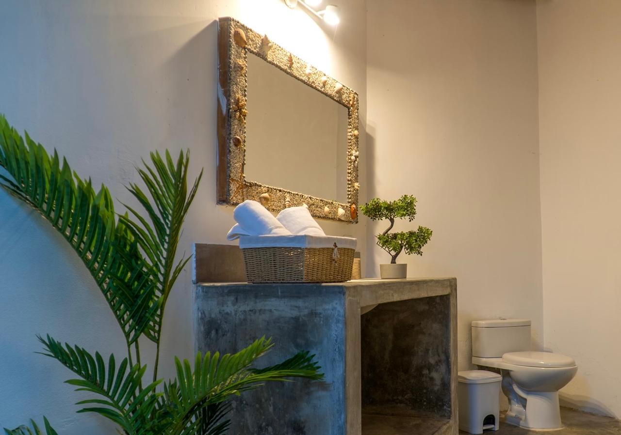 Ensuite stone-finish bathroom with shell-framed mirror, wicker towel basket, and bonsai detail at Bali Lodge