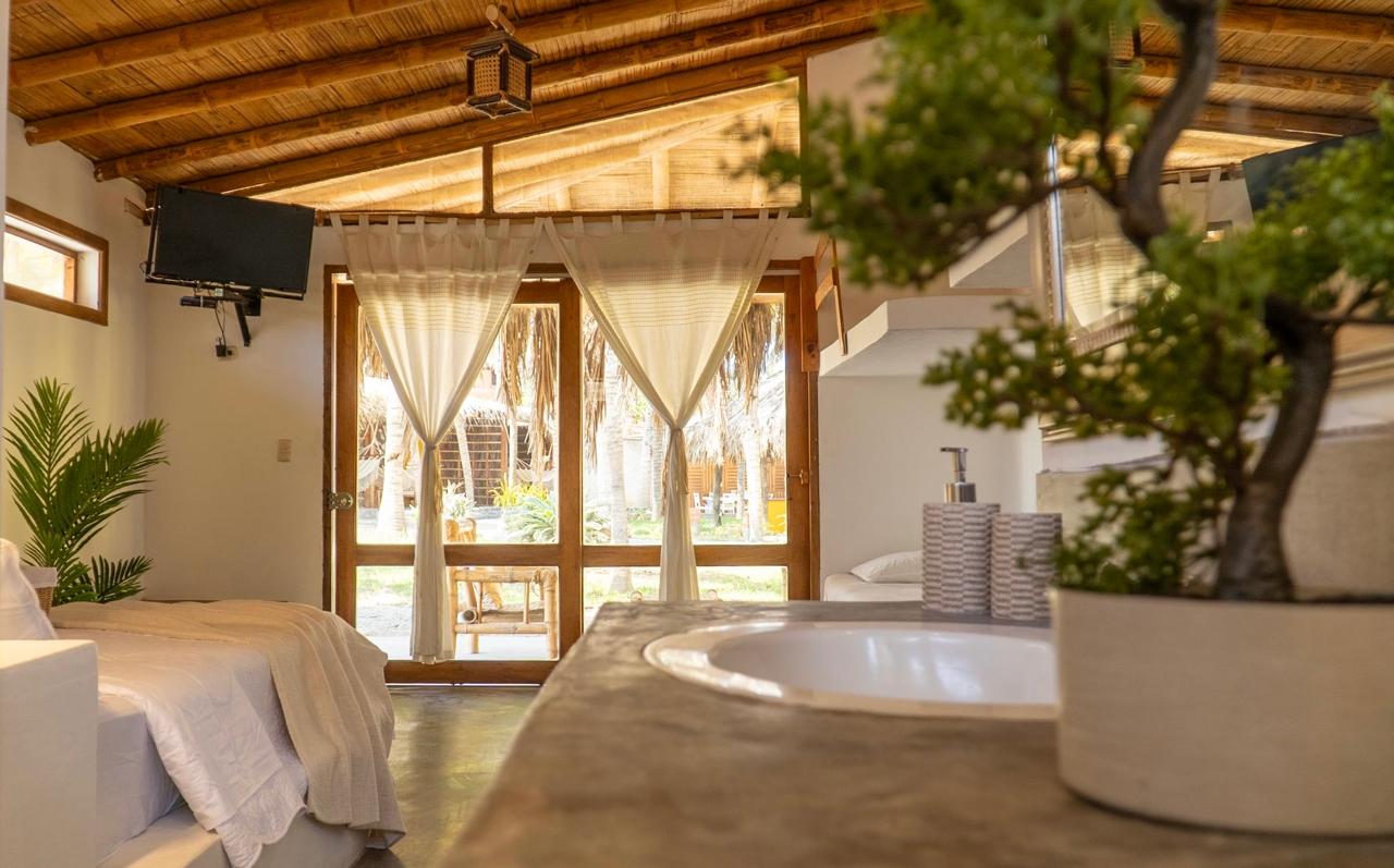 Bali Lodge room interior featuring bamboo-slat ceiling, hanging lantern light, linen curtains, and sunlit garden patio outside