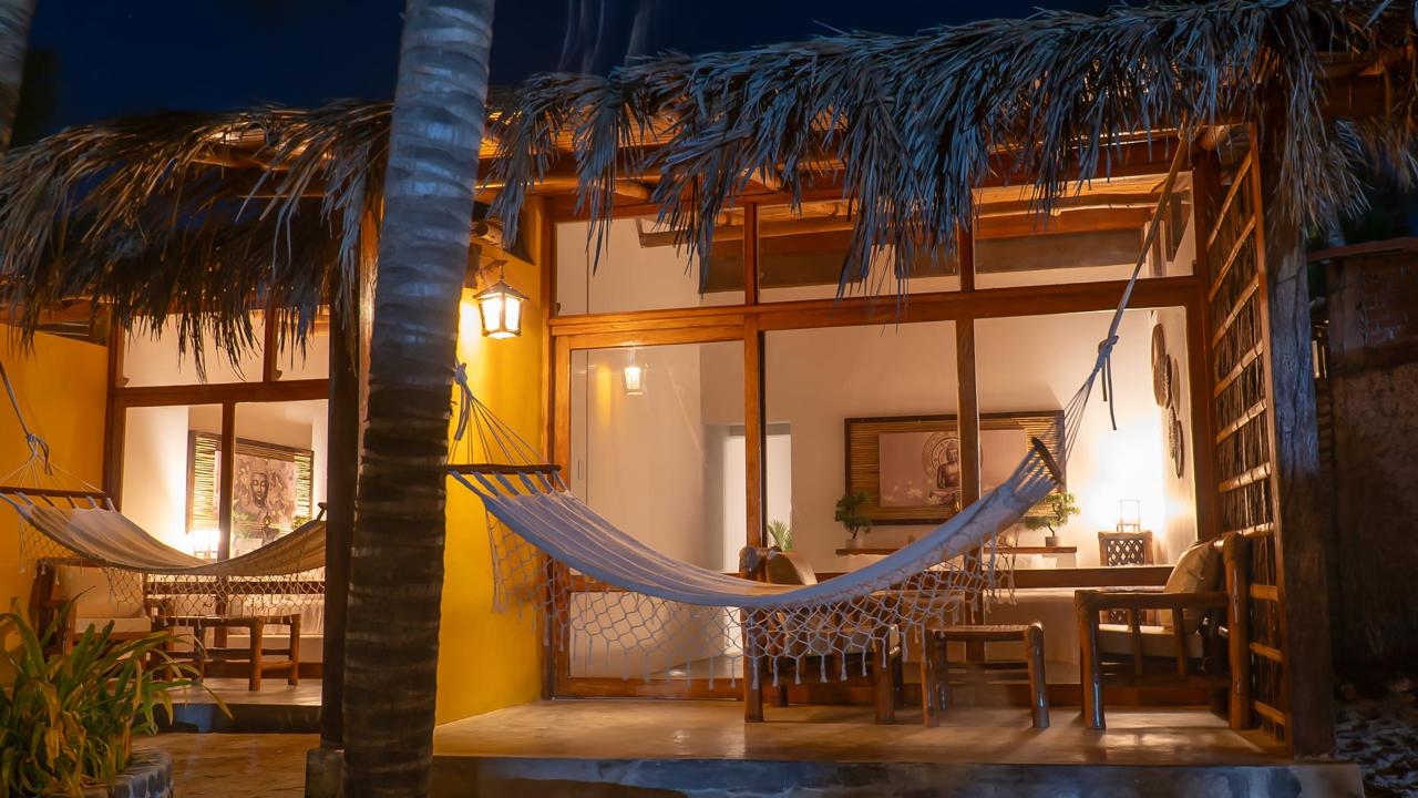 Evening bungalow terrace with woven hammocks, warm lantern lighting, palapa thatch, and coconut palms at Bali Lodge
